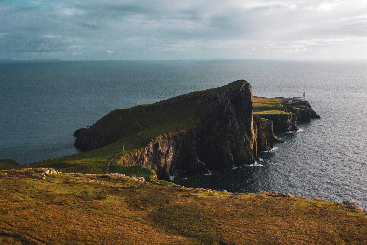 Aerial view of Neist Point lighthouse on the Isle of Skye, Scotland — dramatic sea cliffs and green headland jutting into the Atlantic Ocean