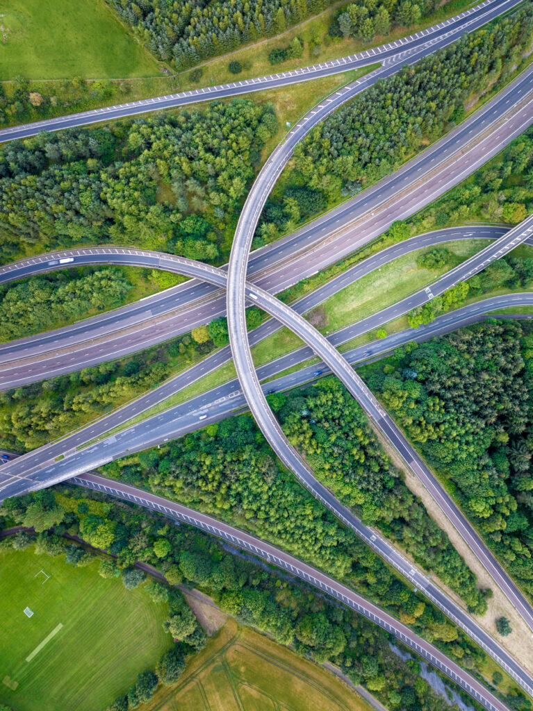 Drone aerial top-down view of a motorway interchange surrounded by green woodland — infrastructure aerial cinematography by OV Production