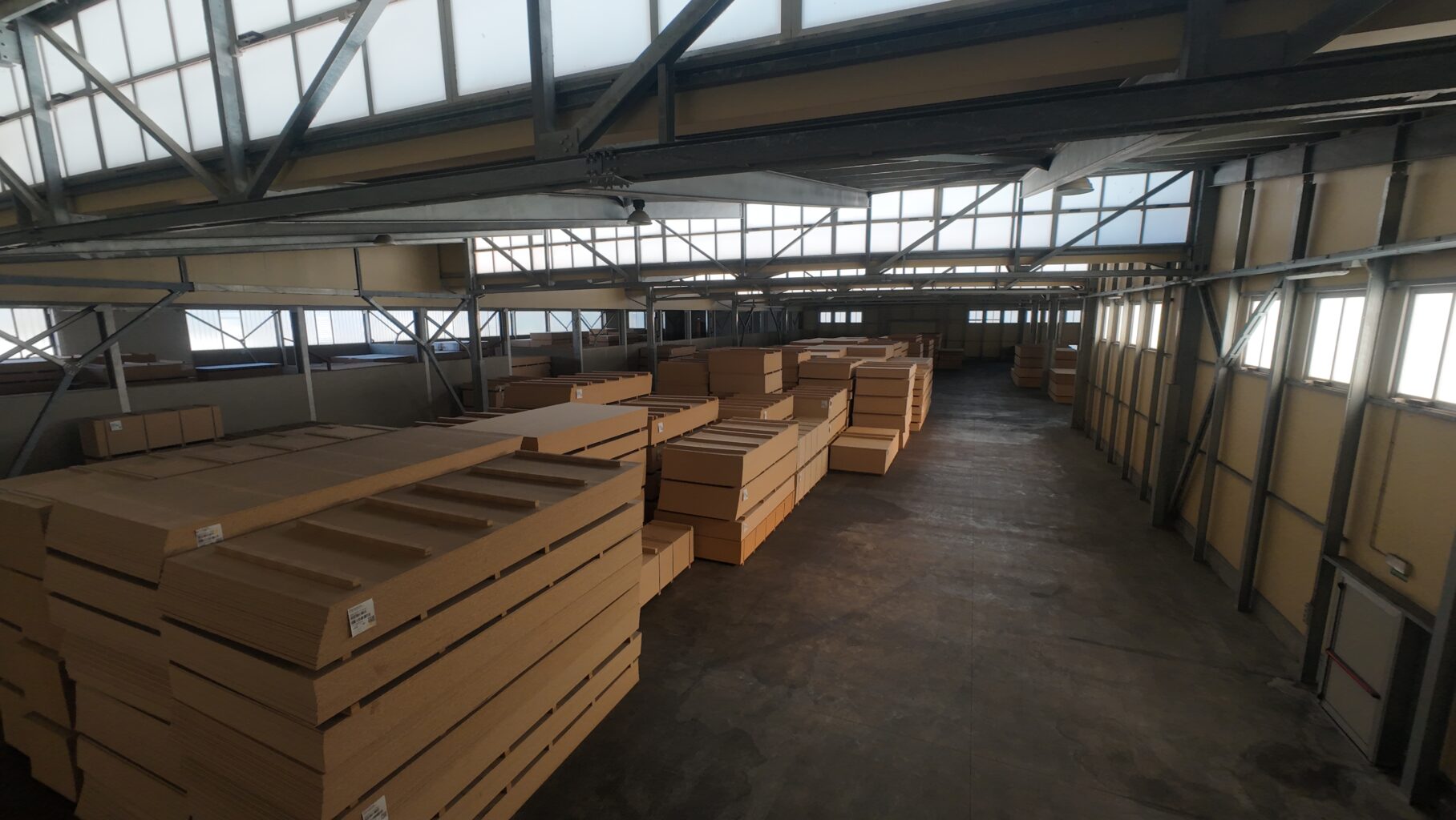 Interior wide-angle view of a large industrial warehouse stacked with timber and MDF panels under a steel-framed roof — industrial videography by OV Production Scotland