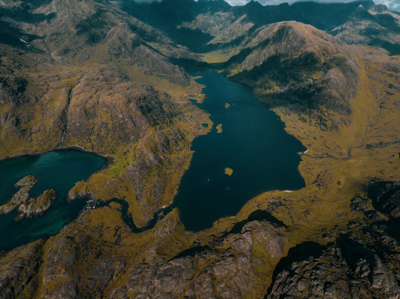 High altitude aerial drone view of a remote Scottish loch nestled between rugged Cuillin mountains on the Isle of Skye — aerial cinematography by OV Production